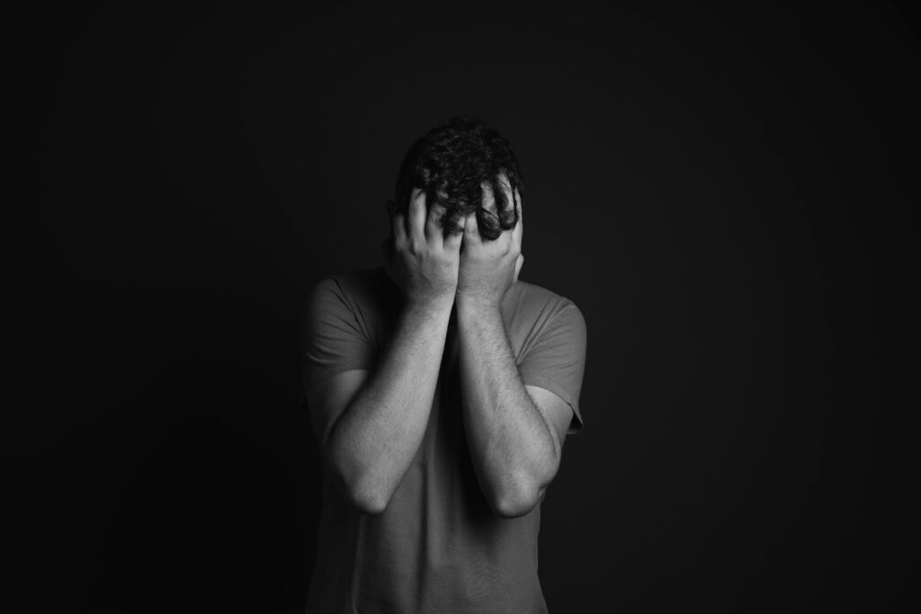 Here are three ALT-text options you can choose from, depending on your SEO need 👇 ✅ Hospital-Focused & SEO-Optimized Alt Text: Man covering his face in emotional distress, representing anxiety, depression, and mental health struggles that require professional psychiatric care.